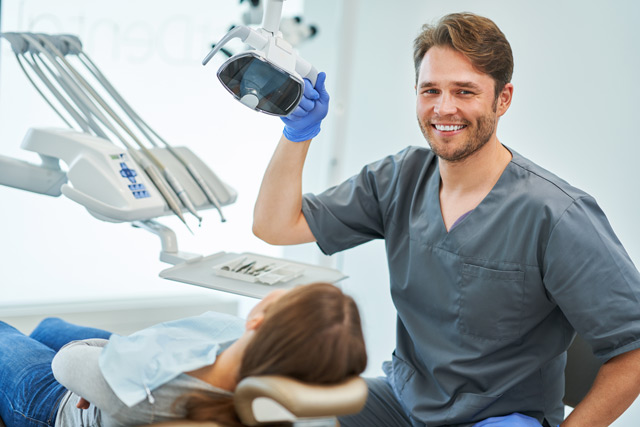 A dentist smiles as he sits with a patient.